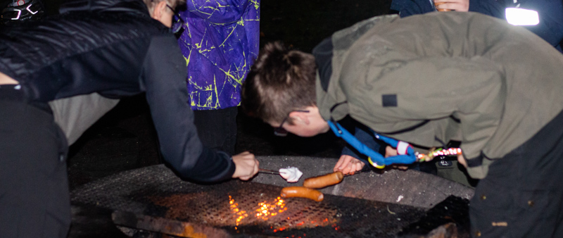 Explorerscouter som grillar korv vid en eldplats